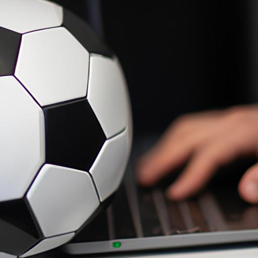 Một người đang đánh máy trên laptop với bóng đá nằm phía sau